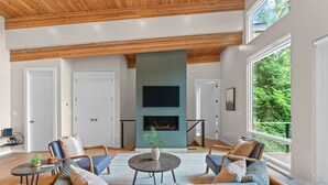 A spacious living room with a large sofa, a coffee table, and a fireplace. There are two doors and a large window with a view of greenery. - Mtn View, 3 Miles to DT AVL, King Bed, Fire Pit (Asheville)