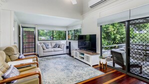 A spacious living room with a sofa, TV, and a large window overlooking greenery. - Nelly's Hidden Cottage (BONGAREE)