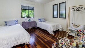 A room with two single beds, a small table with a purple tablecloth, a chair with a floral cushion, and a wooden chair with a woven seat. - Nelly's Hidden Cottage (BONGAREE)