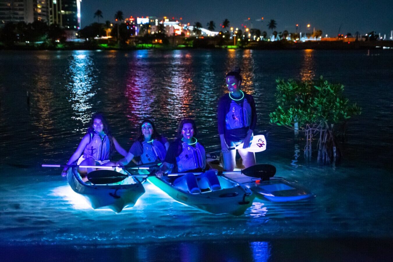 Tre persone in canoa su un corpo d'acqua di notte, con le luci della città sullo sfondo.