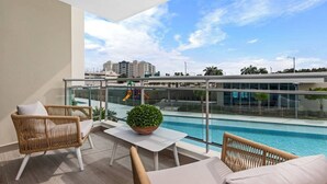A balcony with a pool, wicker furniture, and a view of a playground and buildings. - Poolfront by Isla Verde Beach (Carolina)