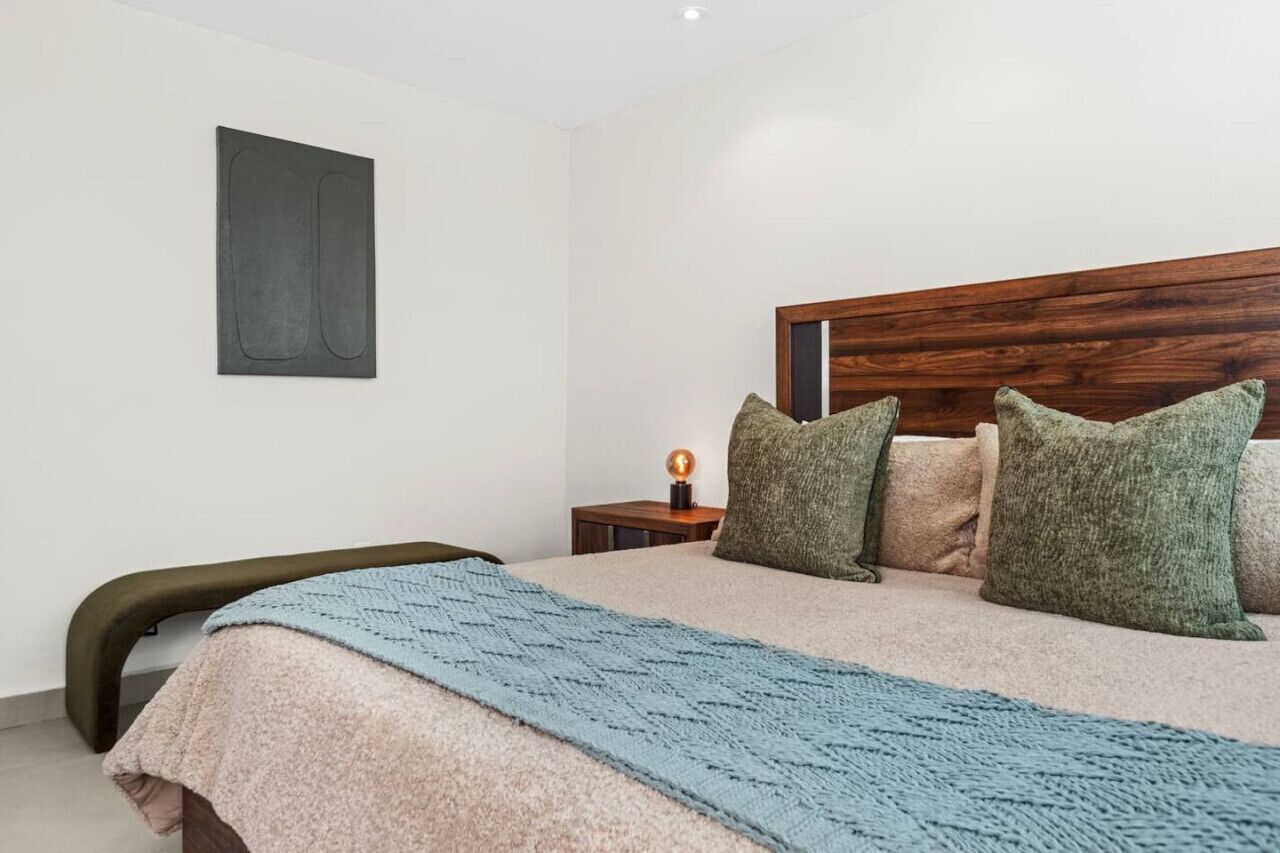 A bedroom with a bed, a nightstand, a wall-mounted artwork, and a bedside lamp.