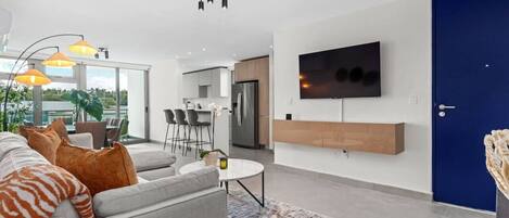 A modern living room with a grey sofa, orange and white cushions, a round coffee table, and a TV mounted on the wall.