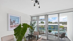 A modern room with a glass table, chairs, a large plant, and a view of a pool and building. - Poolfront by Isla Verde Beach (Carolina)
