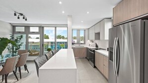 A modern kitchen with a stainless steel refrigerator, wooden cabinets, and a large island with seating. - Poolfront by Isla Verde Beach (Carolina)