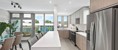 A modern kitchen with a stainless steel refrigerator, wooden cabinets, and a large island with seating.