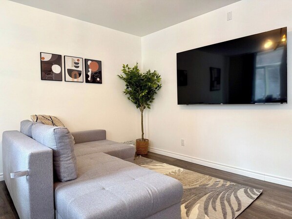 A modern living room with a sectional sofa, a flat-screen TV mounted on the wall, and a potted plant.