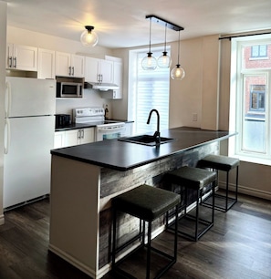 A modern kitchen with white cabinets, a black countertop, a central island with bar stools, and pendant lighting.