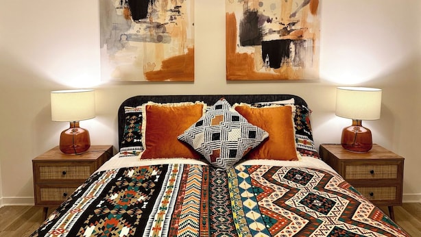 Ein Bett mit gemusterten Betttextilien, zwei Nachttische mit Lampen und abstrakte Wandkunst.