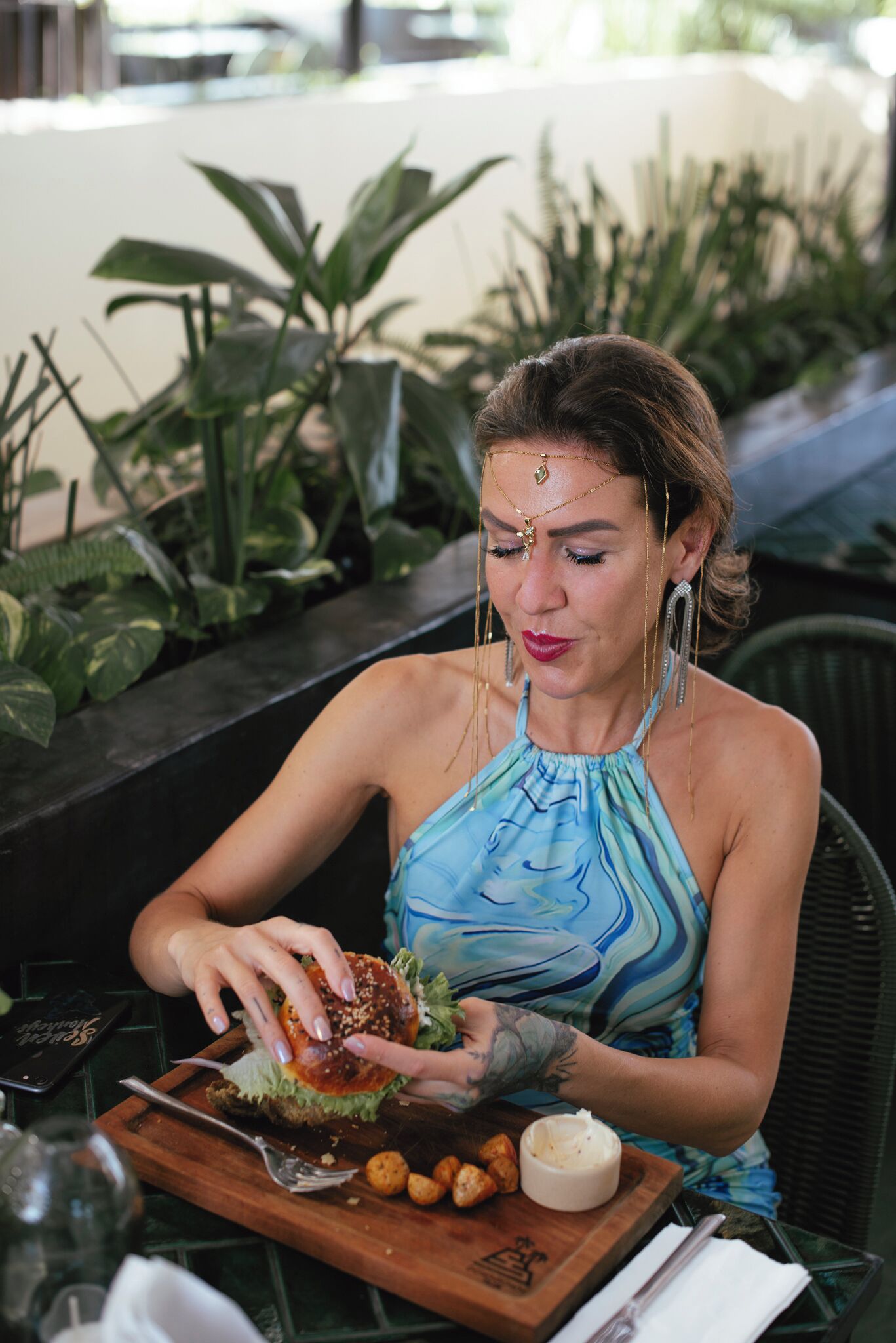A person seated at an outdoor table with a burger, fries, and a small bowl of sauce.