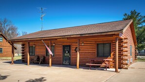 A log cabin with a covered porch, a picnic table, and a flag. - The Frat House at the Riviera Resort in Neillsville, Wisconsin! (Neillsville)