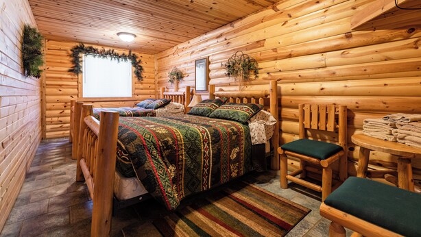 A log cabin bedroom with a bed, two chairs, a small table, and a window. - The Frat House at the Riviera Resort in Neillsville, Wisconsin! (Neillsville)