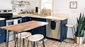 Een moderne keuken met een houten tafel en stoelen, roestvrijstalen apparatuur en een plant in een pot.