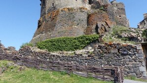 A historic stone castle with a central tower, surrounded by a stone wall and a wooden fence.
