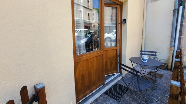 A wooden door with glass panels, a small outdoor table with a chair, and a metal bench.