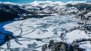 A panoramic view of a snow-covered landscape with a frozen lake, mountains in the background, and a small settlement with buildings along the shore.