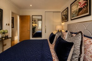 A bedroom with a large bed, a bedside table with a lamp, a mirror, and a framed picture on the wall.