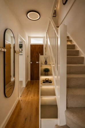 A staircase with a wooden finish, a white wall, and a mirror on the left.