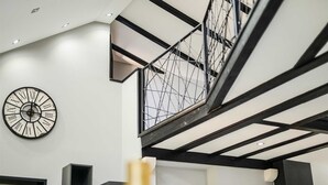 Ein modernes Interieur mit einer großen Wanduhr, einer Treppe mit Metallgeländer und einem Schild mit dem Schriftzug 'HOME' auf einer Theke.