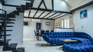 Ein modernes Wohnzimmer mit einem blauen Ecksofa, einem Essbereich mit Tisch und Stühlen sowie einer Treppe mit schwarzen Geländern.