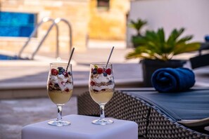 Zwei Dessertgläser mit Früchten und Schlagsahne auf einem Tisch am Pool.