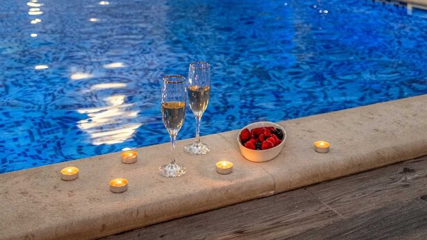 Ein Pool im Freien mit zwei Sektgläsern und einer Schüssel Beeren am Rand.