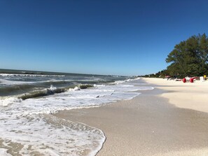 Uma praia com ondas, céu claro e algumas árvores.