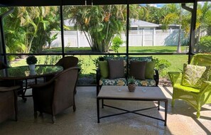 Relax in a serene garden setting with a comfortable patio area featuring wicker chairs and a table.