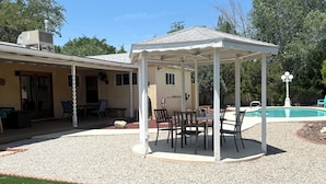 A covered patio area with a table and chairs, a pool, and a house in the background. - Spacious 4-bedroom house with a Pool, AC, WiFi located in Northeast Albuquerque (Albuquerque)