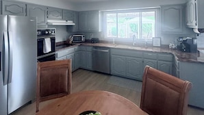 A kitchen with grey cabinets, a stainless steel refrigerator, a microwave, and a sink. There is a dining table with a bowl of green grapes in the center. - Spacious 4-bedroom house with a Pool, AC, WiFi located in Northeast Albuquerque (Albuquerque)
