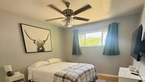 A bedroom with a bed, a ceiling fan, a window with curtains, a mounted TV, and a bedside table with a lamp. - Spacious 4-bedroom house with a Pool, AC, WiFi located in Northeast Albuquerque (Albuquerque)