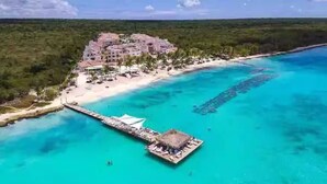 Vista aérea de un resort con playa, un muelle y una estructura de techo de paja.