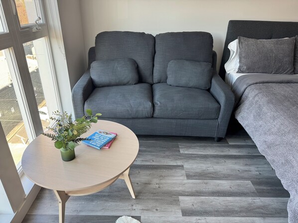 A modern room with a grey sofa, a small round table with a plant, and a bed with grey bedding. - Cozy studio with WiFi, AC, fitness room in lovely midtown of Sacramento. (Sacramento)
