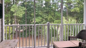 A covered outdoor area with a white railing, a bench, and a wicker chair. - Willow Bend Condo | Close to Barefoot Golf Courses (North Myrtle Beach)