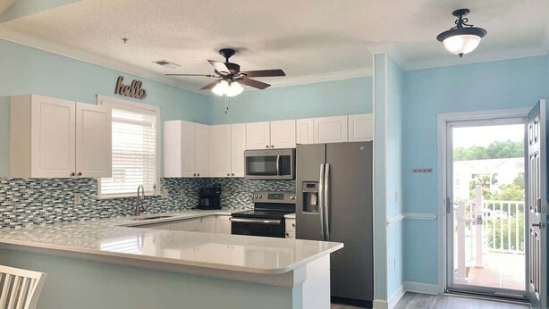 A modern kitchen with white cabinets, a large island, and a view to the outside. - Willow Bend Condo | Close to Barefoot Golf Courses (North Myrtle Beach)