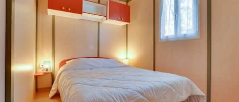 A bedroom with a bed, a nightstand, a window, and built-in red cabinets.