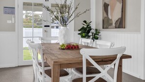A dining area with a wooden table, white chairs, and a vase with branches. - Settle Inn: Broadwater, Pet Friendly (Broadwater)