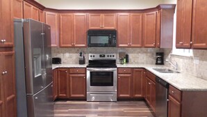 A kitchen with wooden cabinets, a stainless steel refrigerator, a microwave, an oven, and a sink.