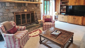 A cozy living room with a stone fireplace, striped armchairs, a wooden coffee table, and a television. - Mountain View Chalet in Boone -10 min. to ASU & Downtown; Pet-Friendly (Boone)