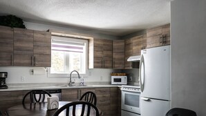A modern kitchen with wooden cabinets, a white refrigerator, a microwave, and a window with blinds. - Le Lodge - Spacious Home (Cochrane)