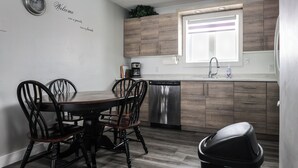 A modern kitchen with wooden cabinets, a stainless steel dishwasher, and a dining area with a wooden table and chairs. - Le Lodge - Spacious Home (Cochrane)