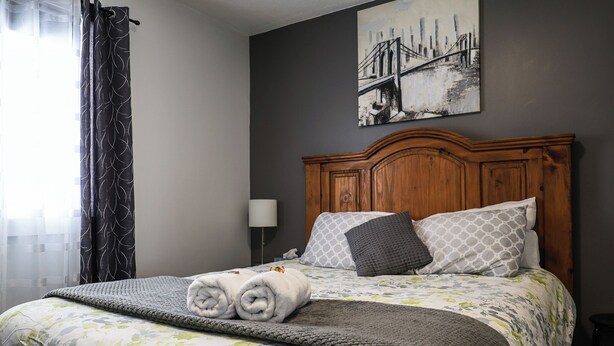 A neatly made bed with floral bedding, a wooden headboard, and two rolled towels. - Le Lodge - Spacious Home (Cochrane)