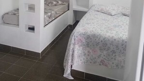 A small, white room with two bunk beds, one with a built-in shelf and the other with a lower shelf. - Pousada Tia Carmem (Ilha Comprida)