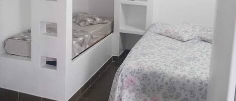 A small, white room with two bunk beds, one with a built-in shelf and the other with a lower shelf.