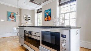 Eine moderne Küche mit Edelstahlgeräten, einem großen Backofen und einer eingebauten Mikrowelle. An den Wänden befinden sich dekorative Gemälde und ein Fenster mit Blick ins Freie.