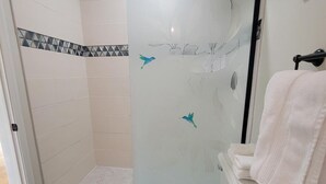 A bathroom with a glass shower door, a white toilet, and a blue rug.