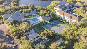 Vista aérea de una zona residencial con casas, una cancha de tenis, una piscina y un lago.