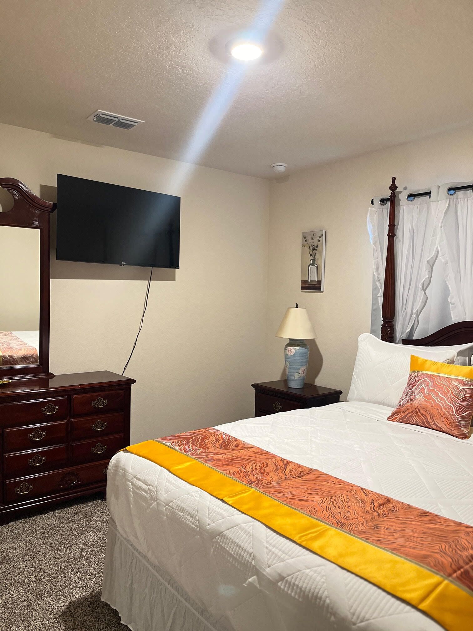 A hotel room with a bed, a dresser, a television, a lamp, and a ceiling light.