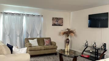 A living room with a sofa, armchairs, a coffee table, a TV, and a painting on the wall.