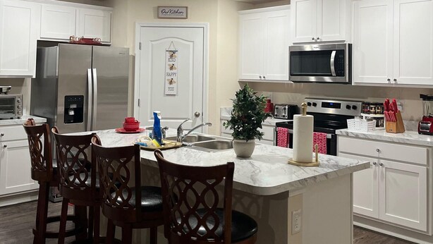 A modern kitchen with white cabinets, stainless steel appliances, a marble countertop, and a central island with bar stools. - Tranquil studio in delightful Palm Coast . DBPR License number DWE2801215 (Palm Coast)
